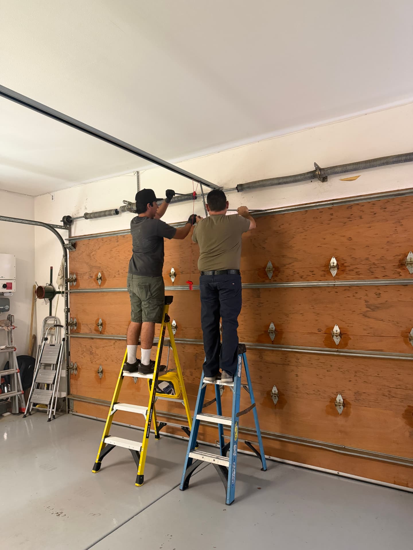Two Daygo Doors technicians replacing torsion springs on a wood garage door